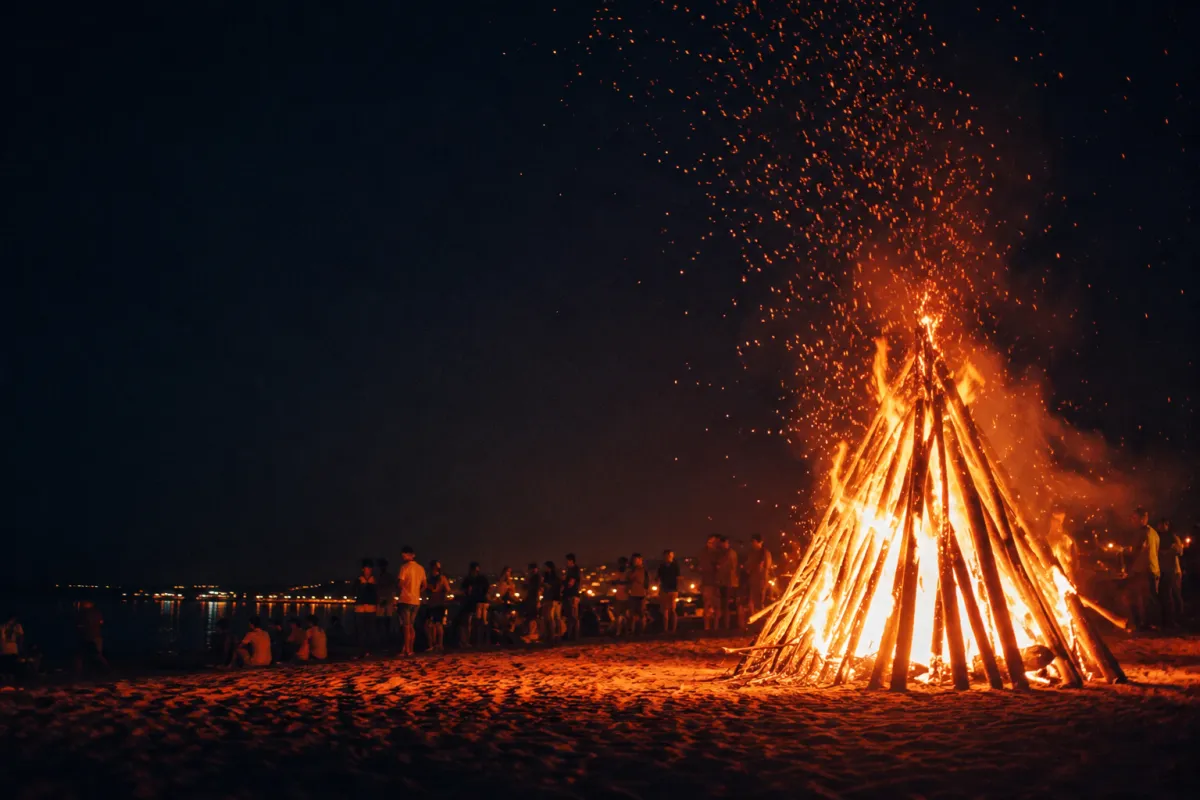 Hoguera de la Revetlla de Sant Joan ardiendo de noche en una playa de Cataluña con chispas elevándose hacia el cielo